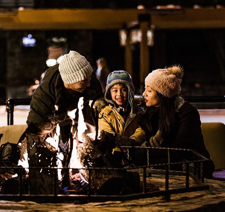 Mother and father sit with son by outdoor fireplace in Lake Tahoe wearing winter hats