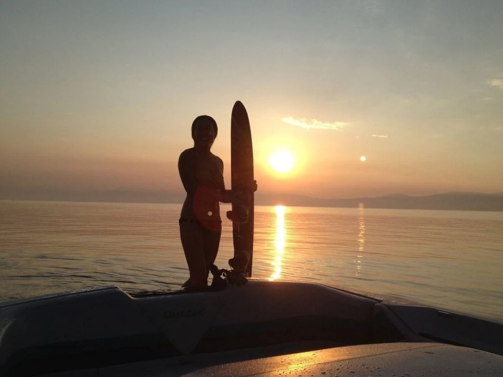 Person standing on the shores of Lake Tahoe with a board at sunset