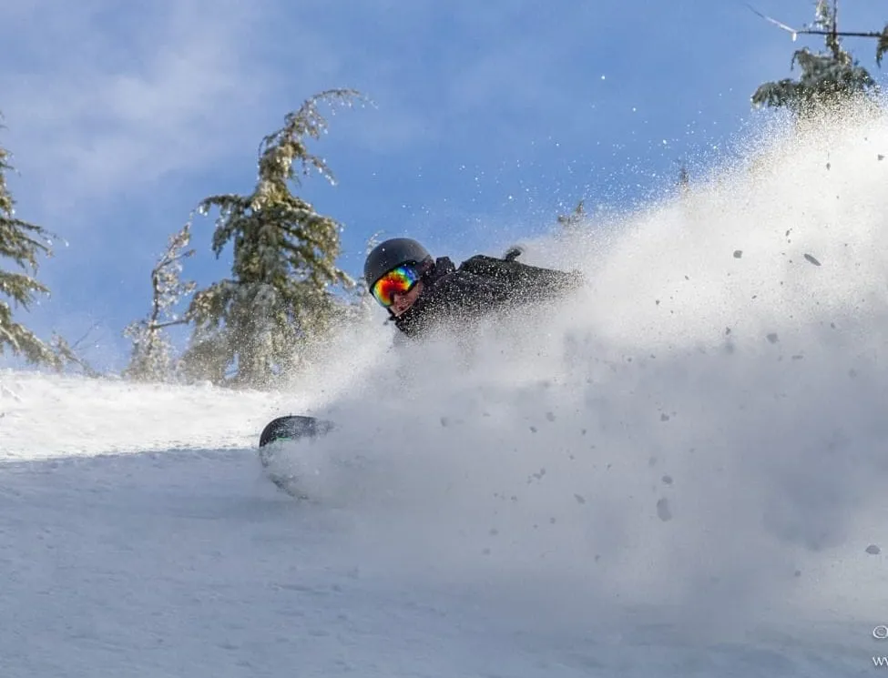 Snowboarder digging in and carving hard in some snowy powder
