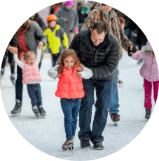 Father holds daughter learning to ice skate amidst other children beginners
