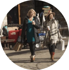 Two woman walking outside holding warm drinks and shopping bags