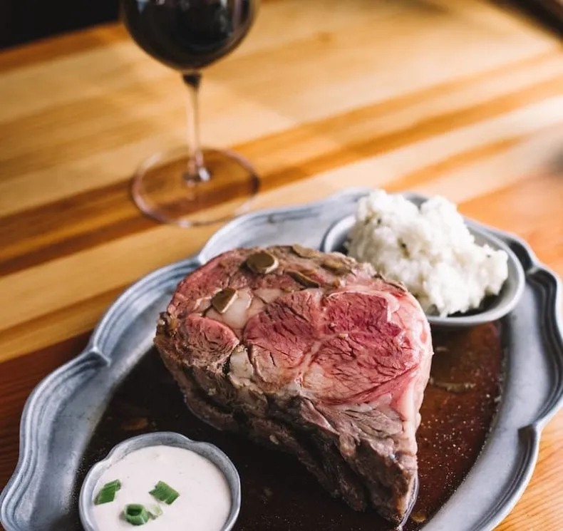 A photo of a are steak, potatoes and horseradish sauce. A glass of red wine looms in the background.