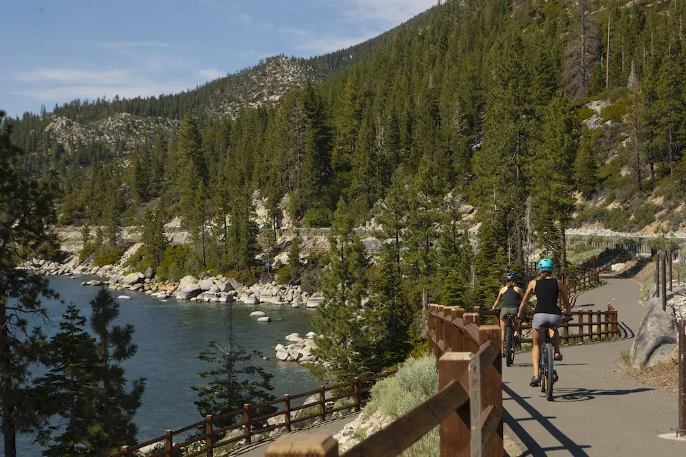 Two women riding mountain bikes on a path next to Lake Tahoe 