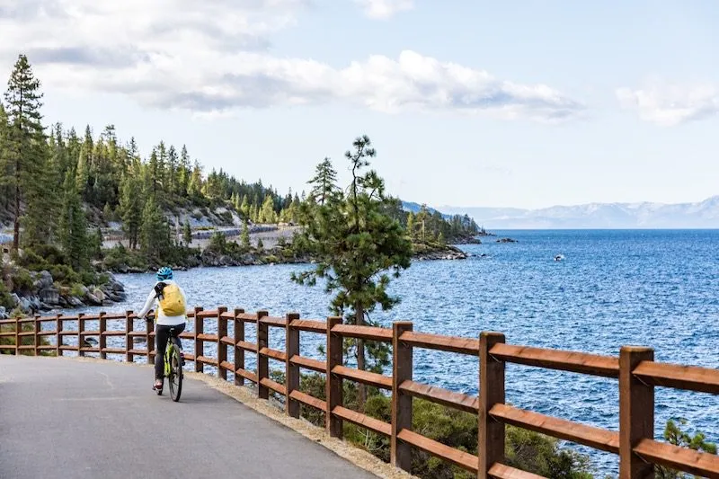 Person riding a bicycle down the paved path next to Lake Tahoe