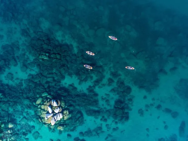 Ariel shot of the greenish blue waters of Lake tahoe with 4 kayaks on it