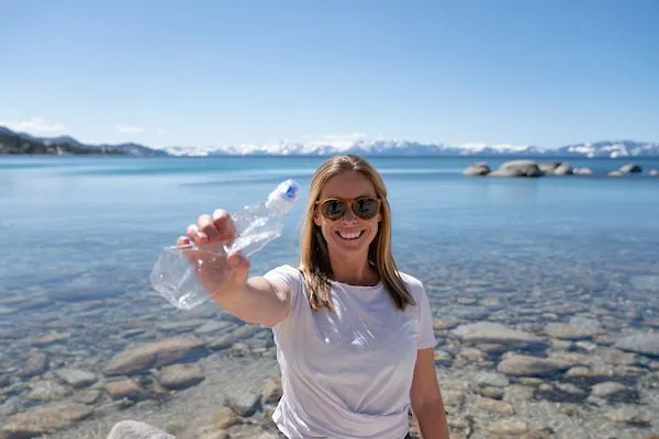 Woman picking up plastic water bottle on the shores of Lake Tahoe