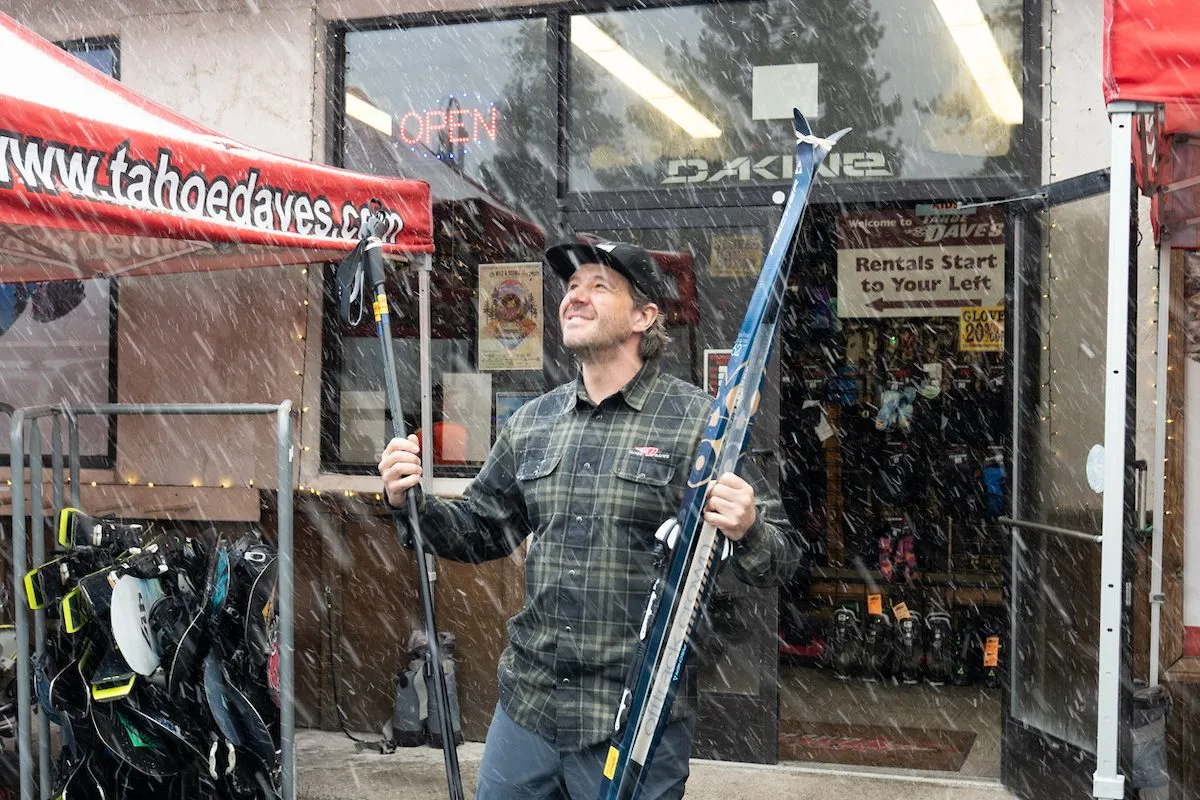 Man standing outside of a ski shop while it's starting to snow